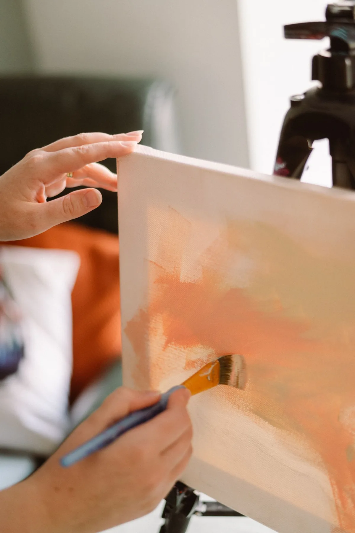 An artist brushing warm orange paint onto a canvas in a studio